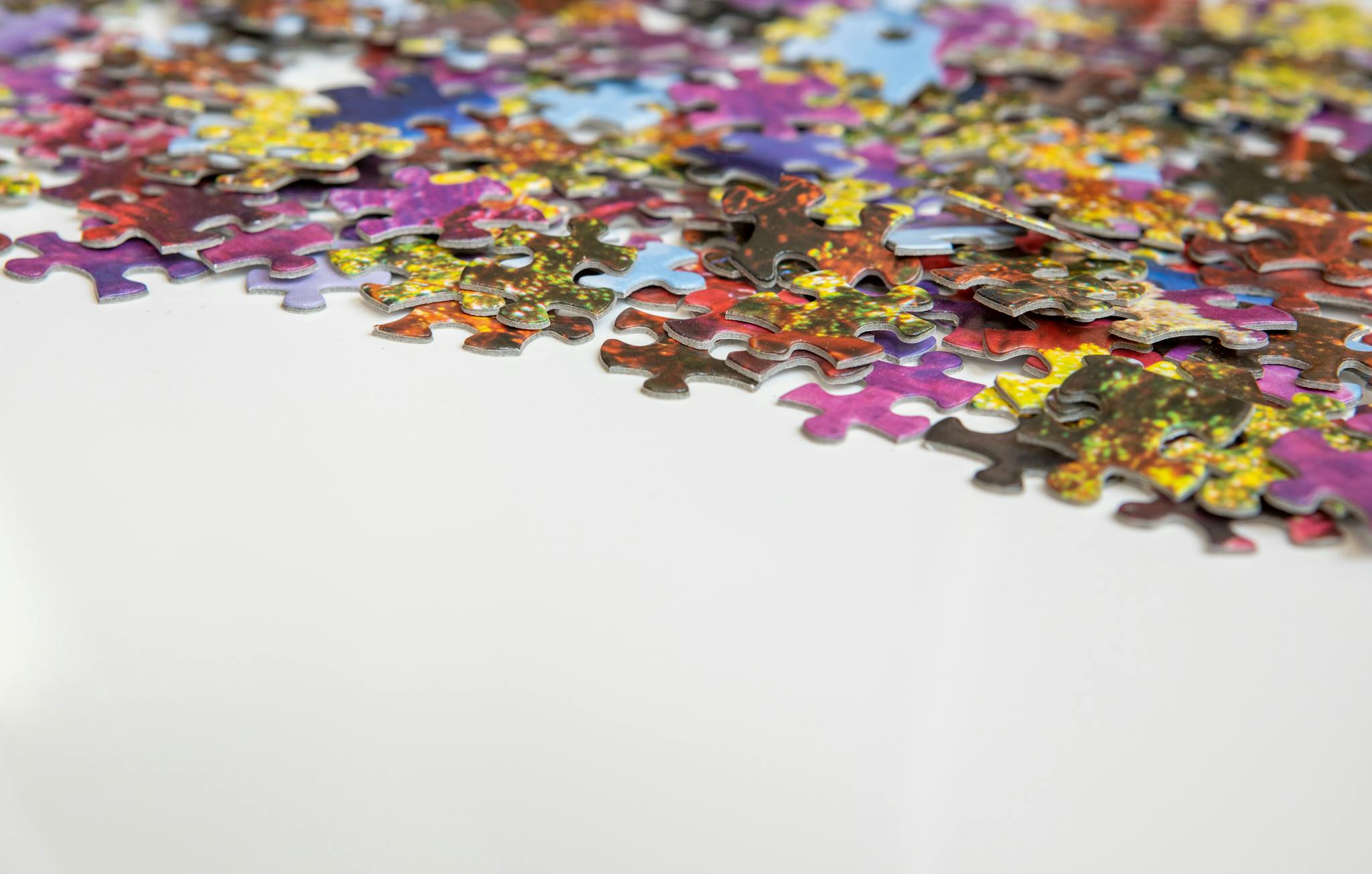 A close-up view of colorful and scattered jigsaw puzzle pieces on a white background.