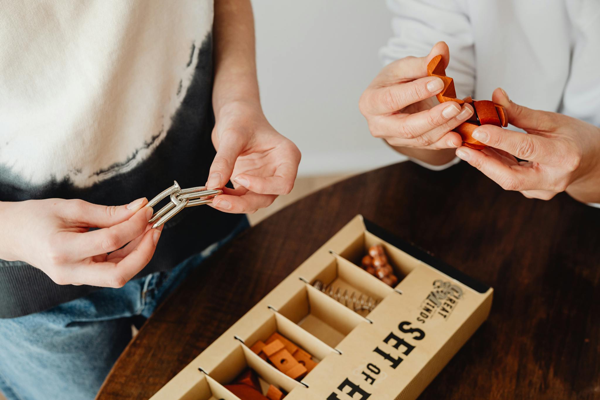 Close-up of hands engaging with metallic and wooden puzzles on a table, promoting creativity and mind games.