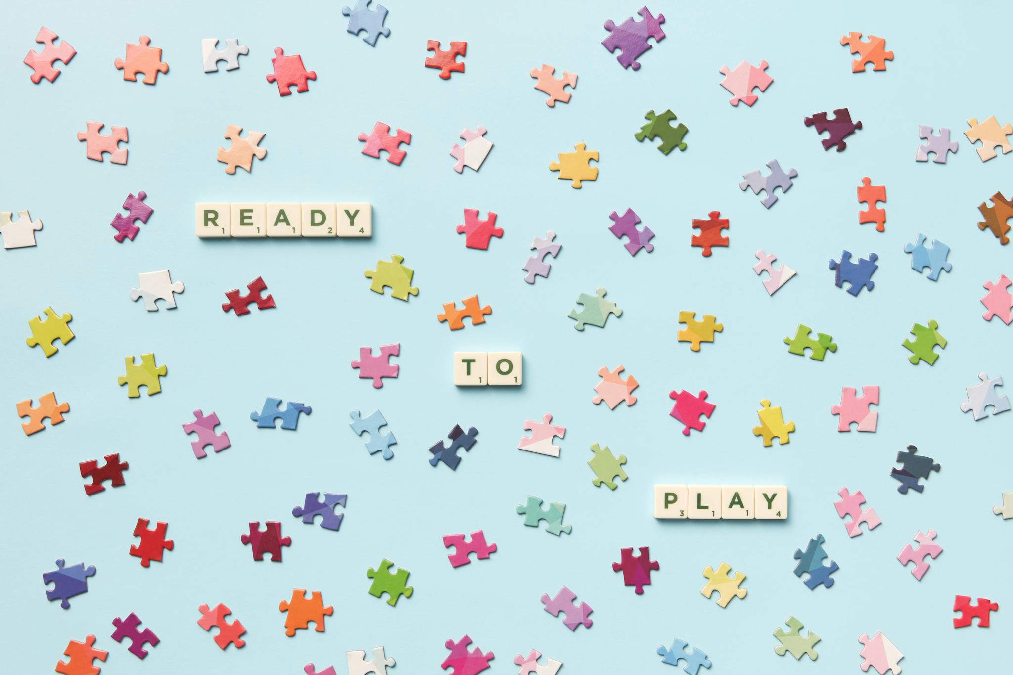 Scatter of colorful puzzle pieces with 'READY TO PLAY' spelled out, on a pastel background.